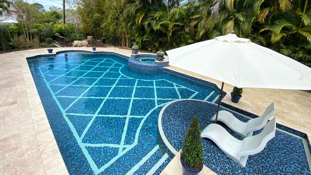 Sun shelf tiles in small format blue tile with two pool loungers and an umbrella set on top of it. It looks out into an all glass tile pool.