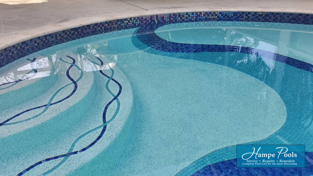 blue and aqua custom glass mosaic in the center of a pool. It matches a beautiful helix-like custom step marker design on the pool steps and the iridescent blue glass tile waterline.