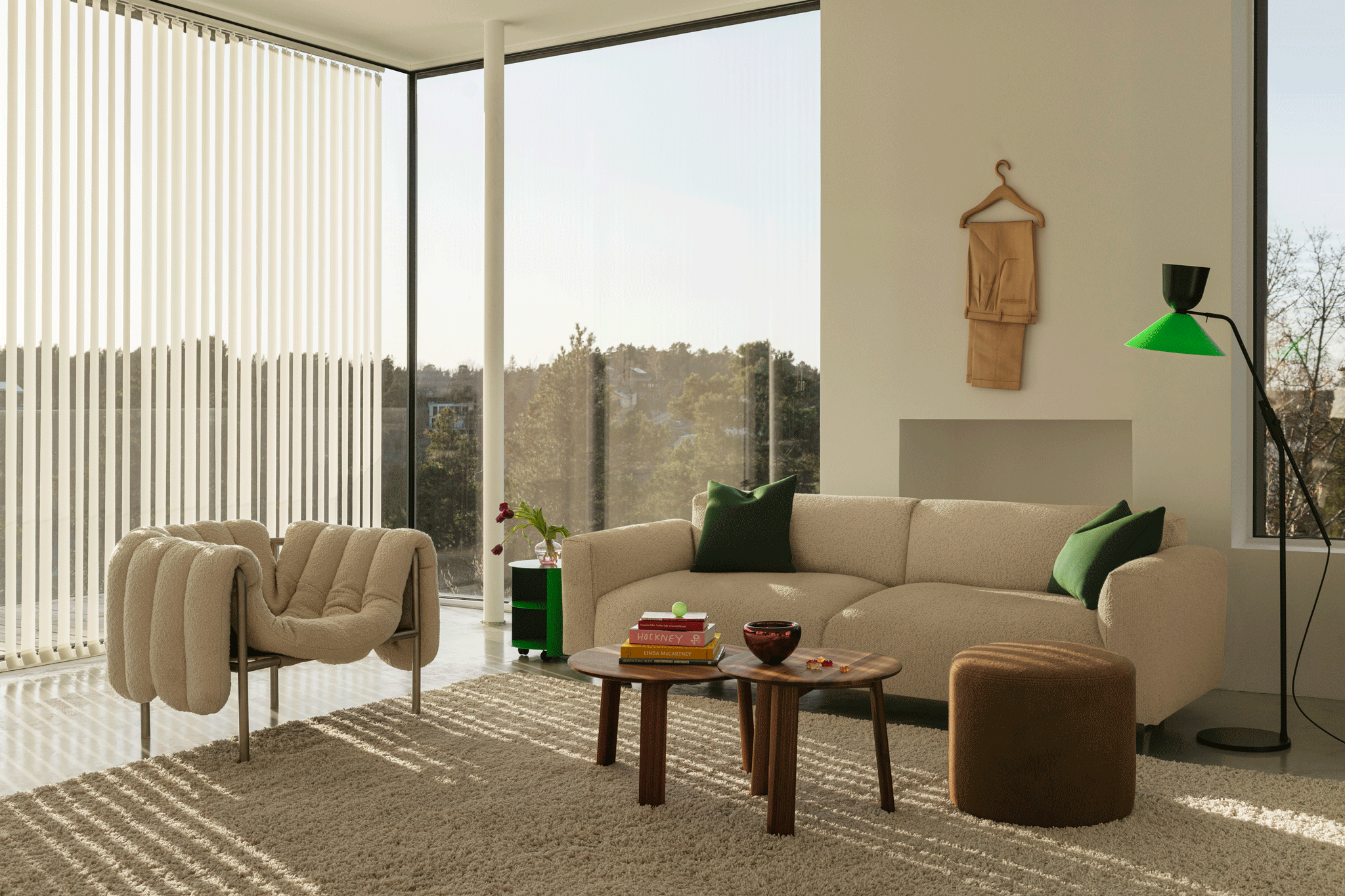 A living room scene featuring a Puffy Lounge Chair in Eggshell / Stainless Steel, Hide Side Table Pure Green, Koti 3-seater Sofa, Alle Round Coffee Tables Set of 2 Walnut, Bon Pouf Round Brown, and an Alphabeta Floor Lamp.