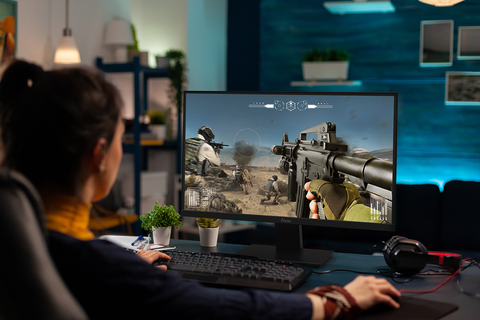Person sitting at a desk, playing a video game on a high refresh rate gamingmonitor.