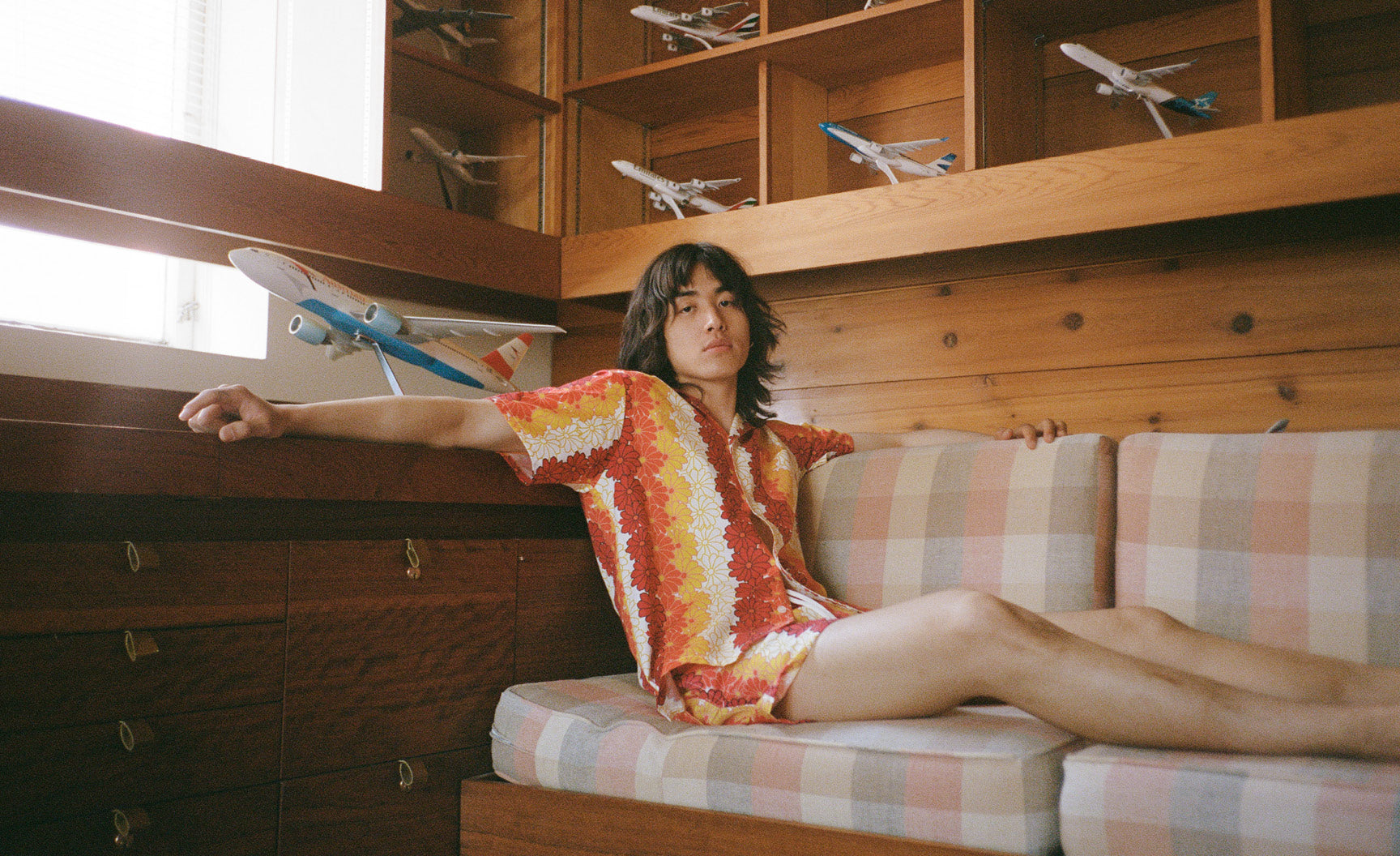 Man sitting on a couch wearing a Hawaiian Tropics camp shirt and matching swim trunks.