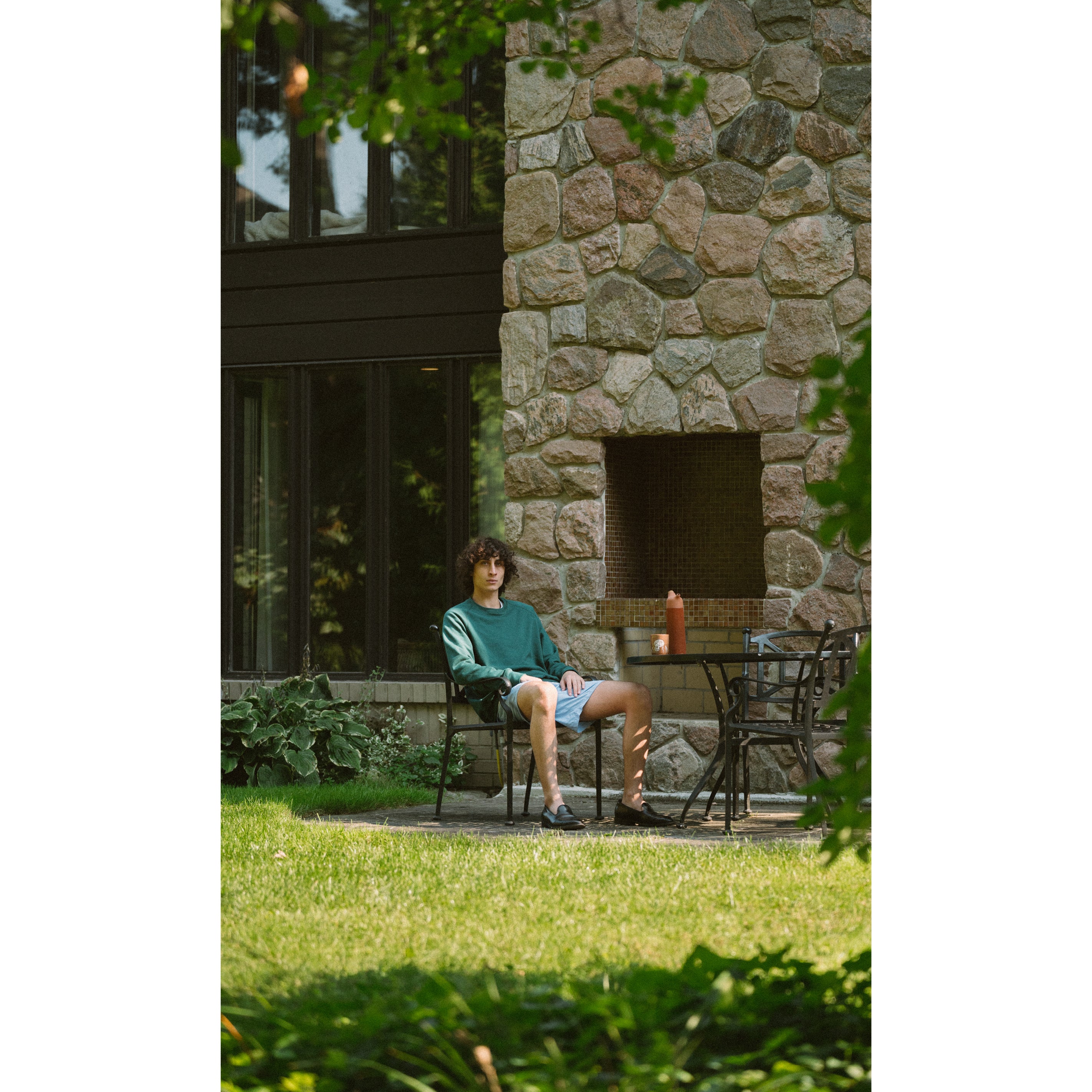 A model sitting and wearing Bather Viridian Green Crewneck and stone swim trunks