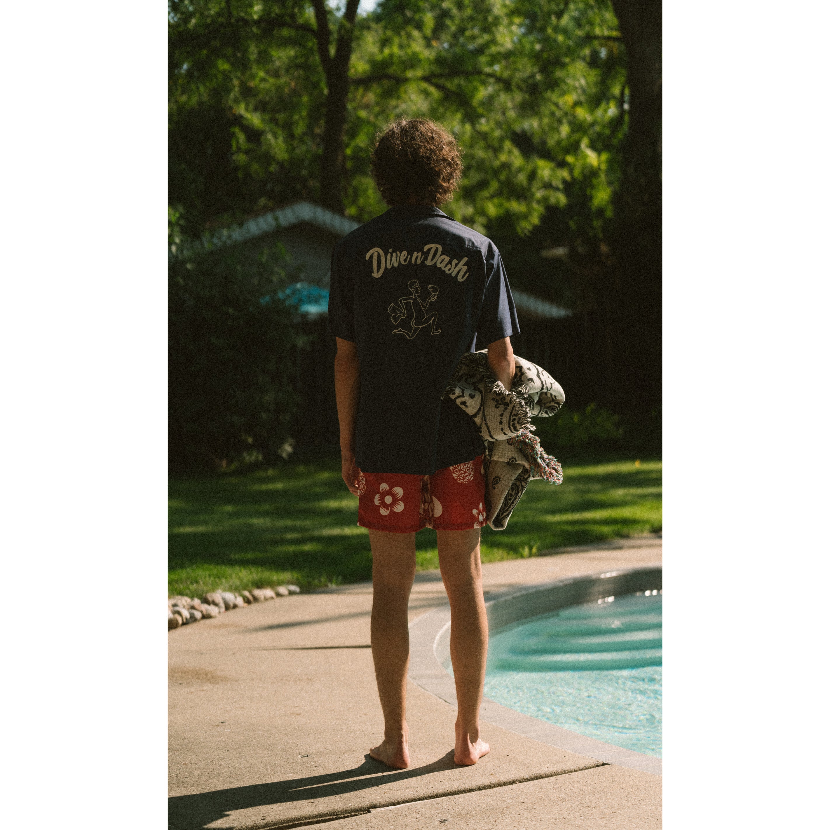 Model wearing navy Bather camp shirt and red coastal floral swim trunks