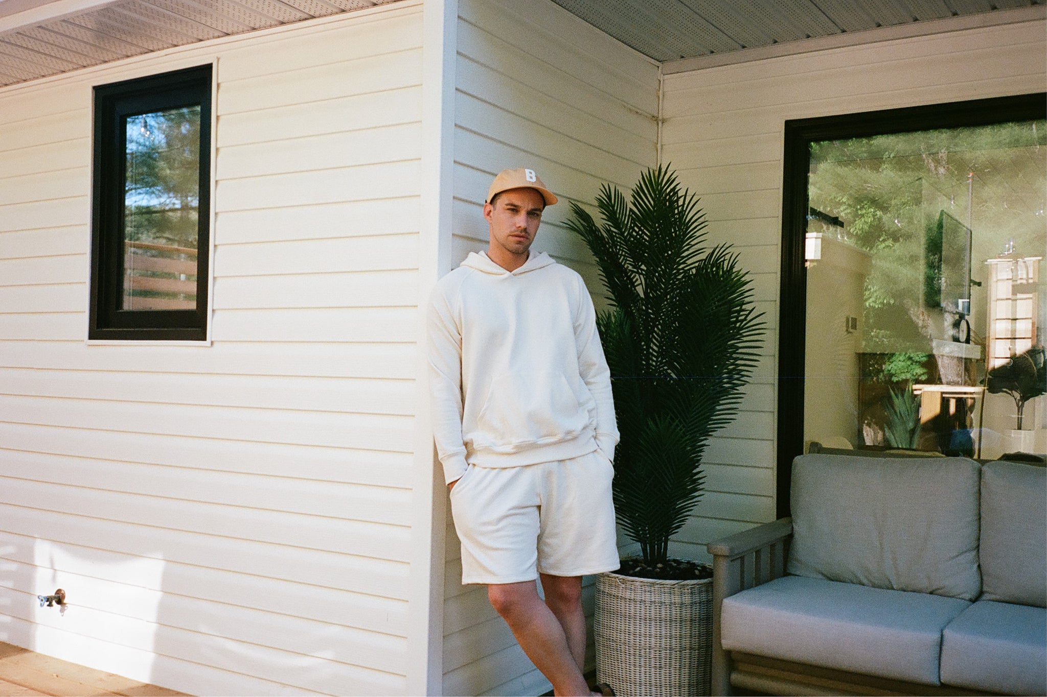 Man wearing cream coloured sweatshirt and sweatshorts with a mustard yellow cap