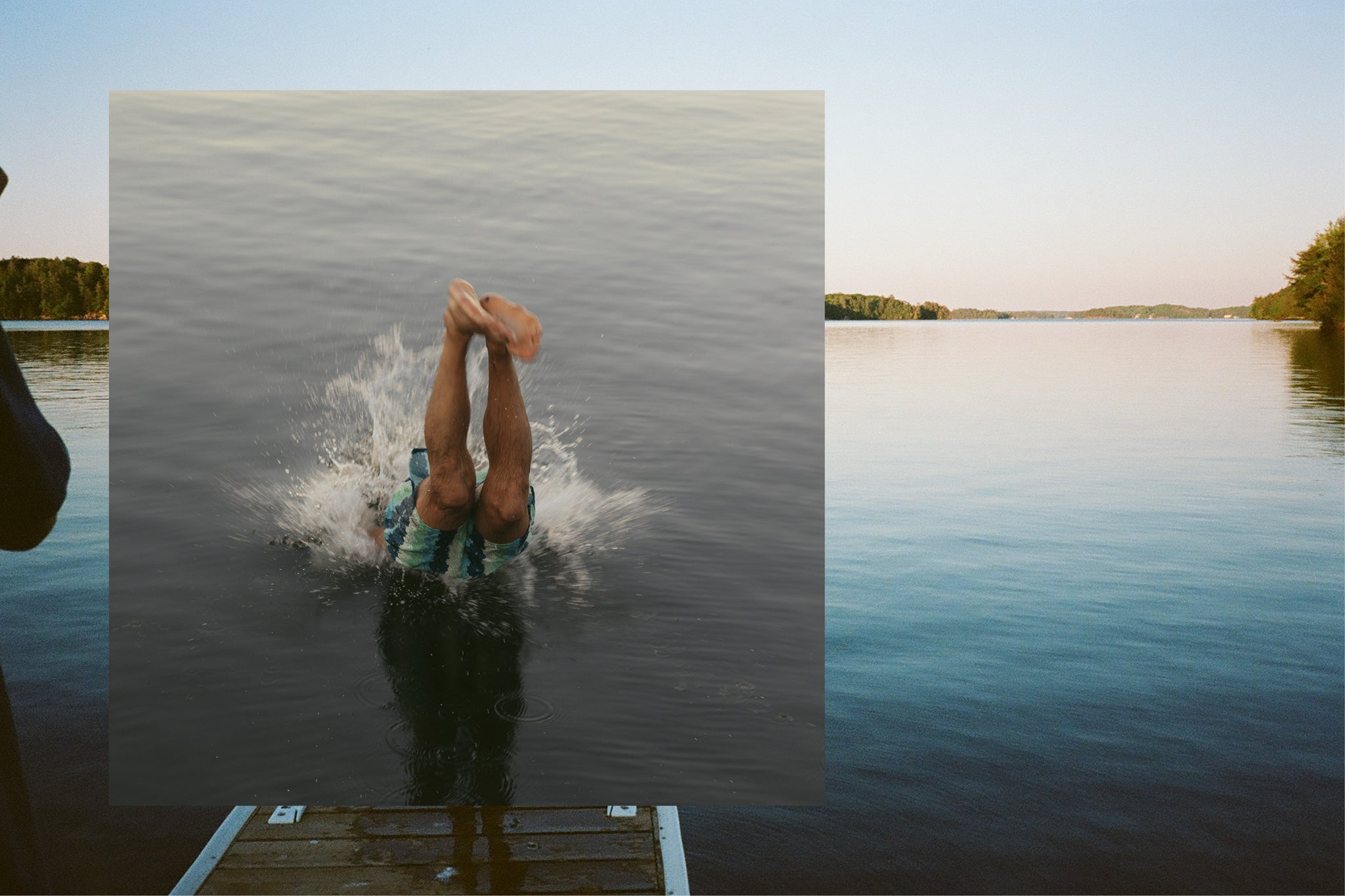 Man diving off a dock into a lake while the sun sets