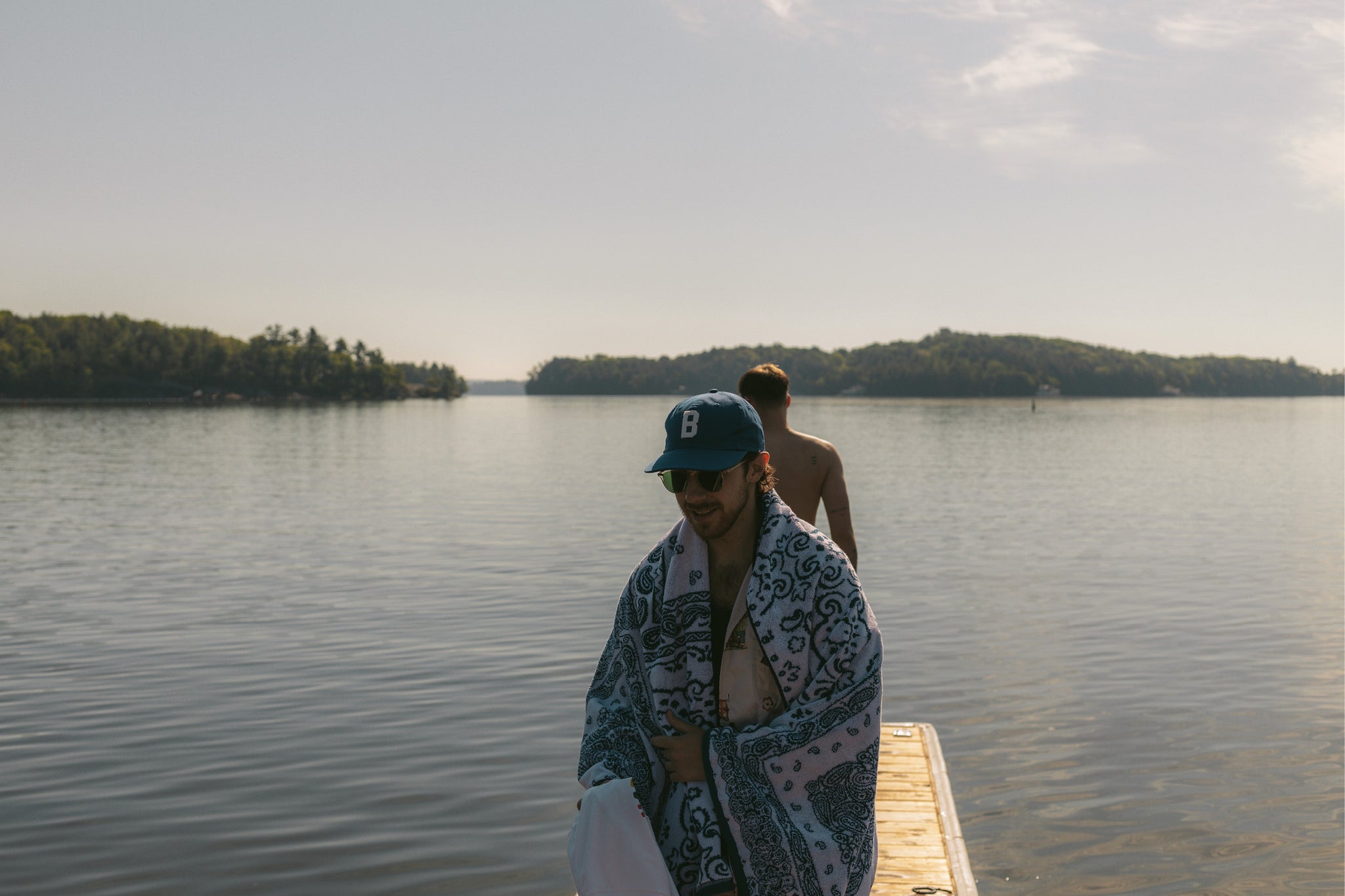 Man standing on a cottage lake dock with a bandana printed towel wrapped around himself