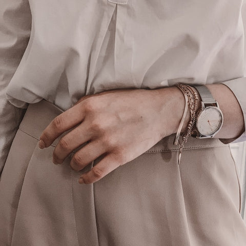 Close up onto a person's waist. They are wearing a braclet and a silver watch on their hand. They are also wearing a white dress shirt and beige slacks