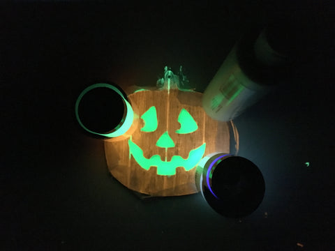 Glowing wooden jack o'lantern sign, with several objects placed along the edges of the wax paper