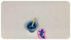 Silicone mold with resin curing inside, alongside the measuring cup containing sapphire blue pearl resin mixture