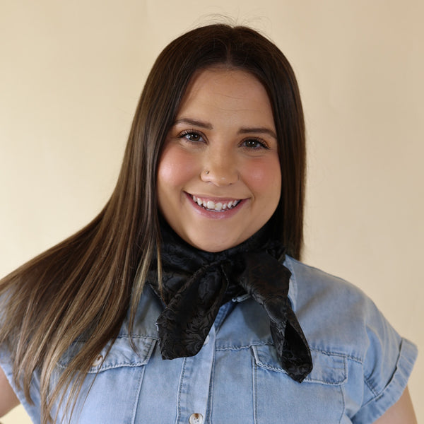 Brunette model wearing a blue dress with Jacquard Black print scarf tied around her neck. Model is pictured in front of a beige background.