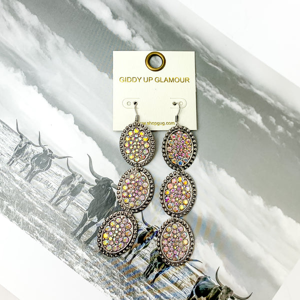 Three tier silver tone oval shape dangle earrings with ab crystals. Pictured on a black and white western picture.