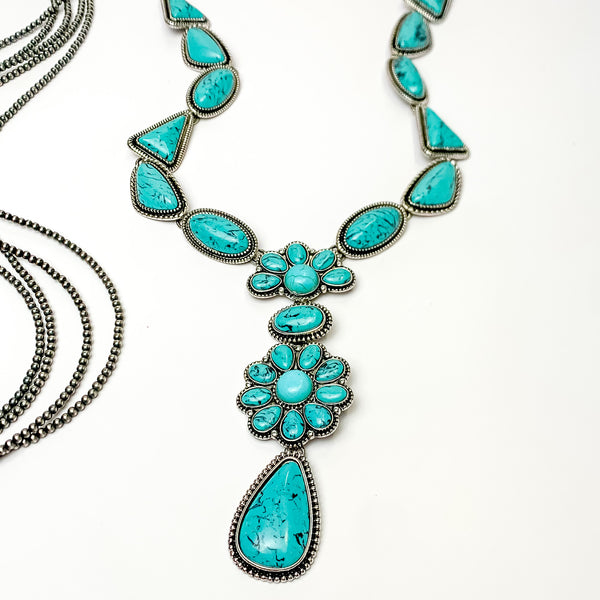 Multi stoned long necklace in turquoise with a dangling flower cluster. Pictured on a white background with Navajo pearl stands.