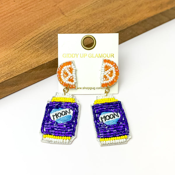 Beaded Blue Beer Can Earrings with Orange Slice Studs. Pictured on a white background with a wood piece at the top.