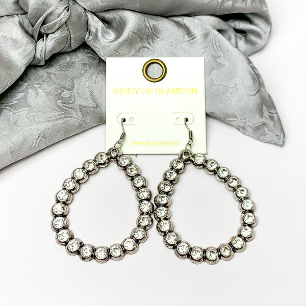 Open Teardrop Earrings with Clear Crystal Outline in Silver Tone. Pictured on a white background with silver fabric at the top.