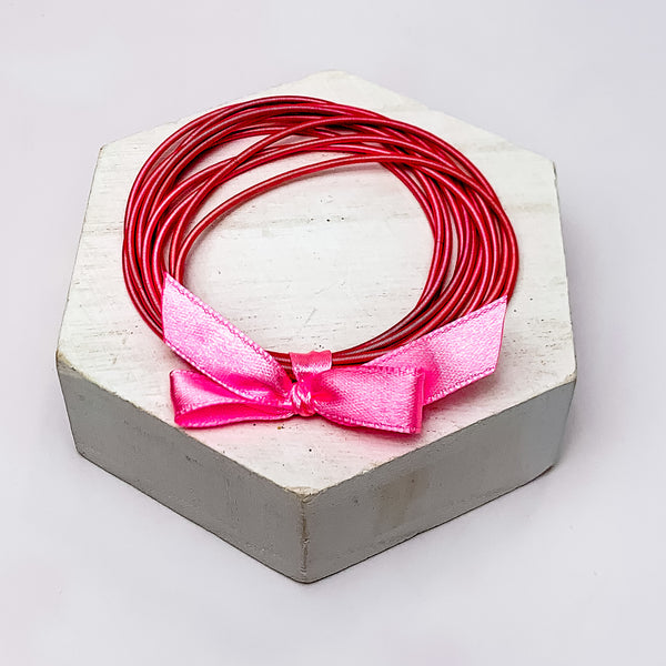 Guitar String Bracelets with Bow in Dark Pink. Pictured on a white background sitting on top of a white block.