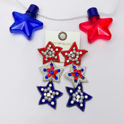 Red, White, And Blue Three Tier Star Earrings. Pictured on a white background with a red and blue star behind the earrings for decoration.