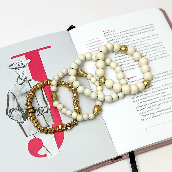 Set of Four | Stretchy White Ivory Beaded Bracelets featuring a Gold Tone Bracelet. Pictured on a white background. Bracelets are laying on top of an open book.