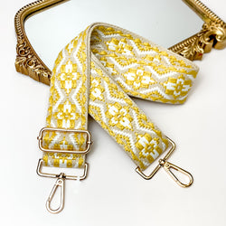Beige canvas purse strap with white and yelow embroidered aztec design. This purse strap includes gold accents. This purse strap is pictured partially laying on a gold mirror on a white background.