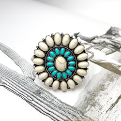 Ivory and Turquoise Oval Stone Concho Hinge Cuff Bracelet. Pictured laying on top of an open book with a western picture behind the bracelet. 