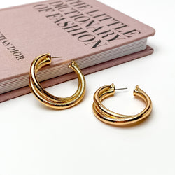 Gold, textured twisted hoop earrings. These earrings are pictured on a white background with one hoop is laying against a mauve colored book. 