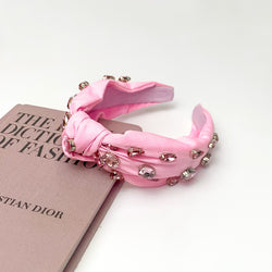 Crystal Detailed Knot Headband in Light Pink. Pictured on a white background with the headband laying on a pink book.