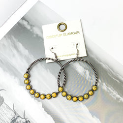 Forever Twisted Hoop Earrings with Stones in Yellow. Pictured on an open book with a gray sky in the background.