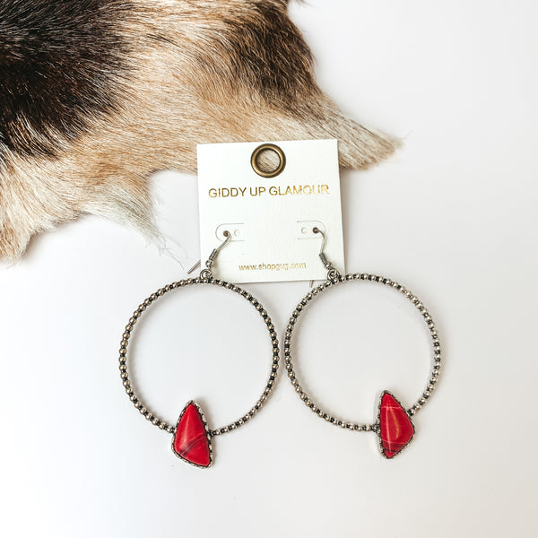 Silver Tone Textured Hoop Earring with Red Stone. Pictured on a white background with faux animal fur to the left.