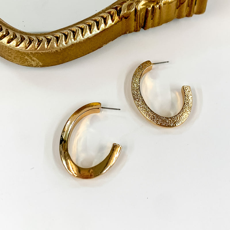 Thick Oval Gold Tone Hoop Earrings. Pictured on a white background with a gold frame at the top of the picture.