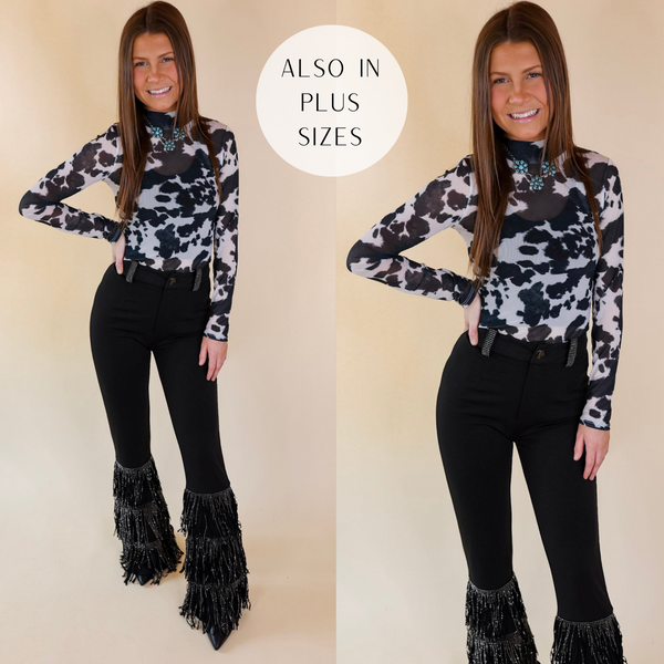 Model is wearing a long sleeve bodysuit that is a black and white cow print. Model has this long sleeve bodysuit paired with black bell bottom pants, black boots, and turquoise jewelry.