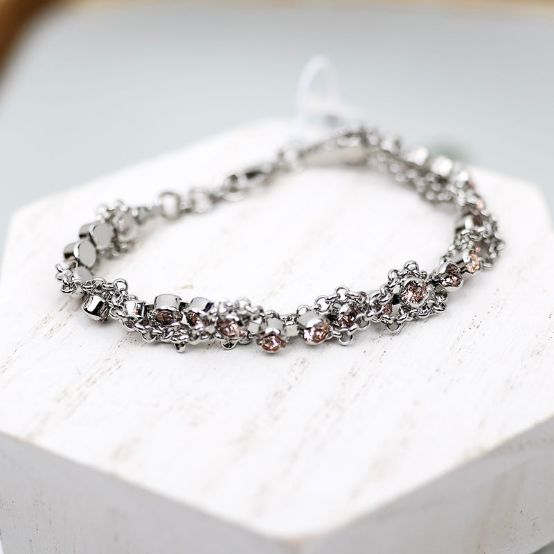 A silver-tone tennis bracelet with blush pink crystals and chain detailing. Pictured on a white background.