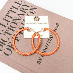 Pictured are circle orange hoop earrings with gold beads around it. They are pictured with a pink fashion journal on a white background.