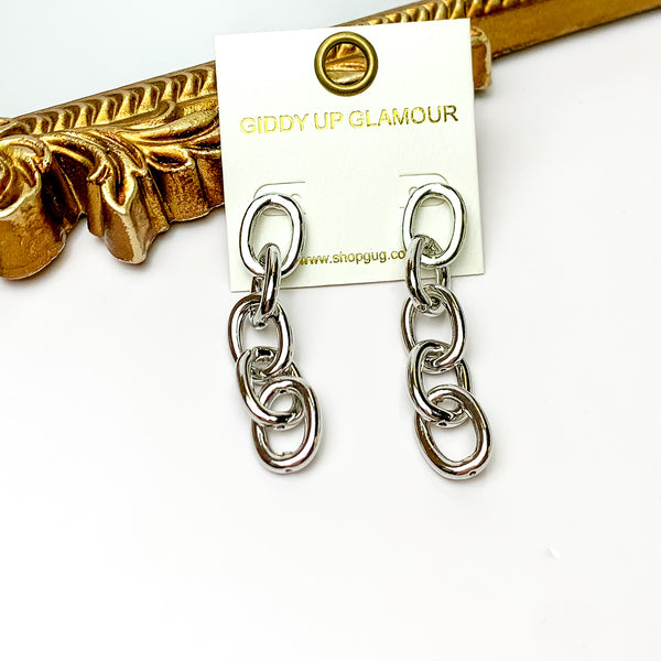 Silver tone chain dangle earrings. Pictured on a white background with a gold frame through it.