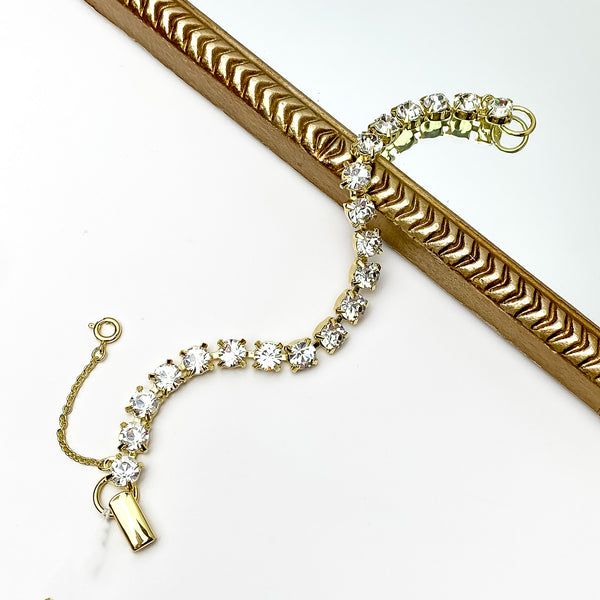 Gold tennis bracelet with clear crystals all around it. Pictured on a white background with a gold piece through it.
