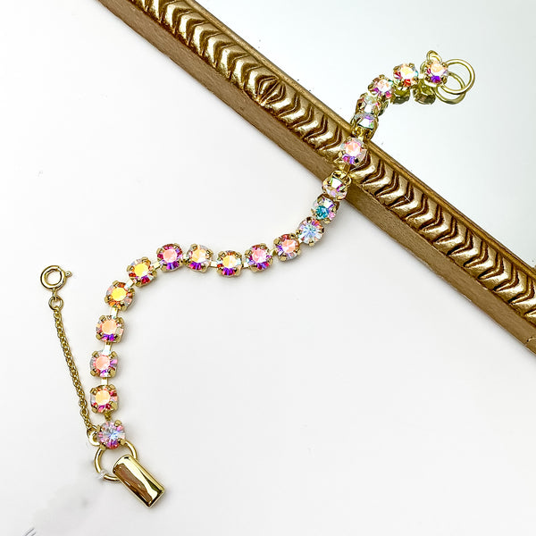 Gold tennis bracelet with Aurora Borealis crystals. Pictured on a white background with a gold frame through the middle. 