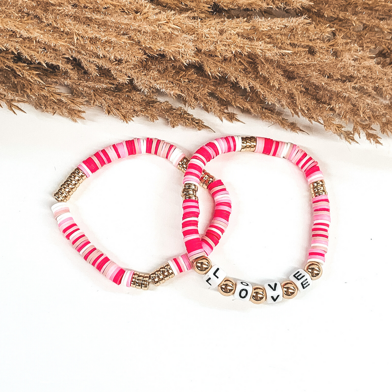 Two bracelets that has a mix of pink colors and white disk beads. On one bracelet, you have three sections of gold disc beads. On the other bracelet you have three smaller section of gold disc beads and then letter beads that spell out "LOVE" with gold spacers in between. These bracelets are pictured on a white background. 
