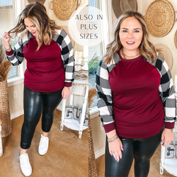 Model is wearing a red top with buffalo plaid long sleeves. Model has it paired with faux leather pants, white sneakers, and gold jewelry.