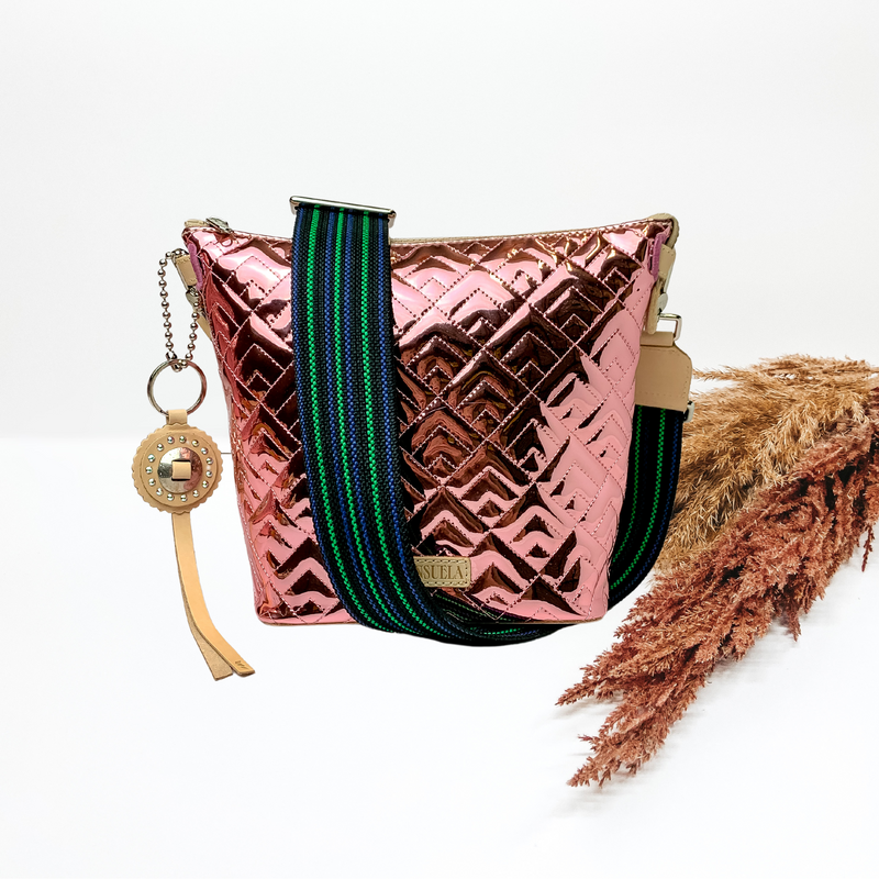 A pink wedge bag is sitting in the middle of the picture. Background is solid white with pompas grass to the right of the purse.   