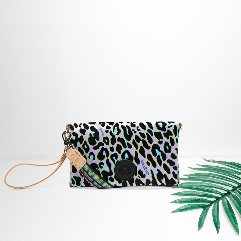 A purple leopard print purse with a multi cross body strap. Pictured on white background with a palm leaf.