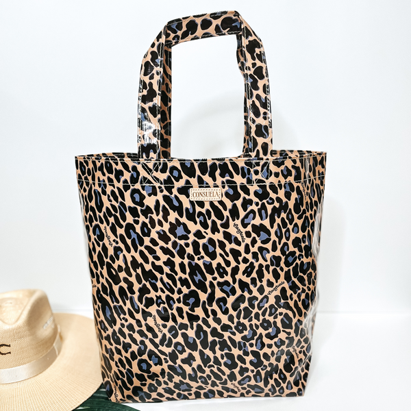 A large size leopard print bag with handles. Pictured on white background with palm leaf and straw hat.