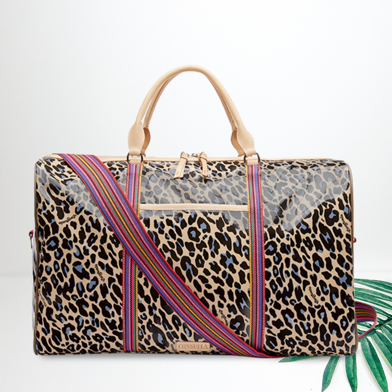 Centered in the picture is a weekender bag in blue cheetah. To the right of the tote is a palm leaf, all on a white background.