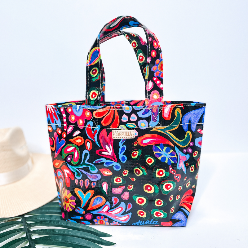 A small size black bag with multi color designs. Pictured on white background with a palm leaf and straw hat.