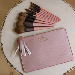 A blush pouch is laid in the bottom of the picture with 11 different sized makeup brushes across the top of the pouch in pink and brown. Background is white.  