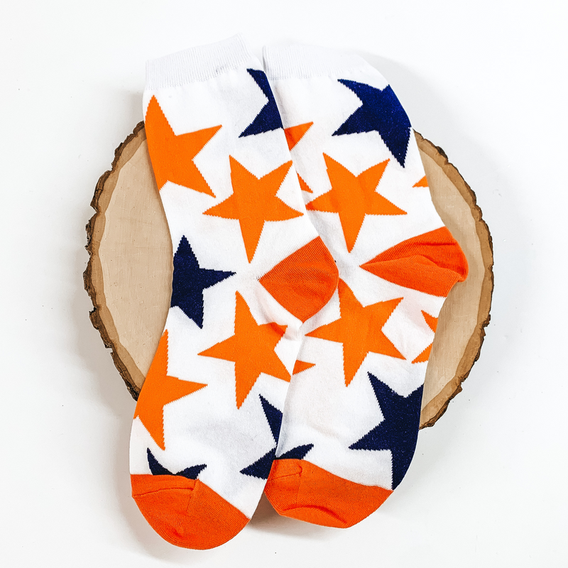 White ankle socks with a navy and orange star print design. These socks are pictured on a piece of wood on a white background. 