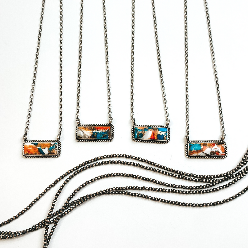 Four silver chain necklaces with rectangle bars that have a spiny oyster and turquoise remix stone. These necklaces are pictured on a white background with silver beads under the necklaces. 