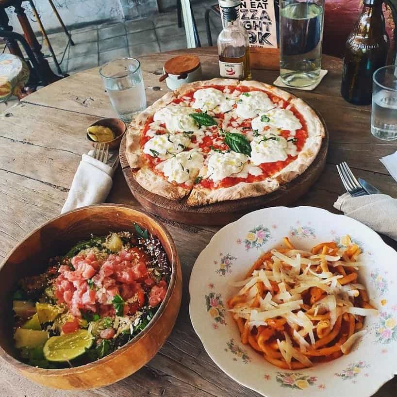 A dining table at La Baracca in Canggu, Bali, featuring plates of rustic pizza, vegetables and salad.
