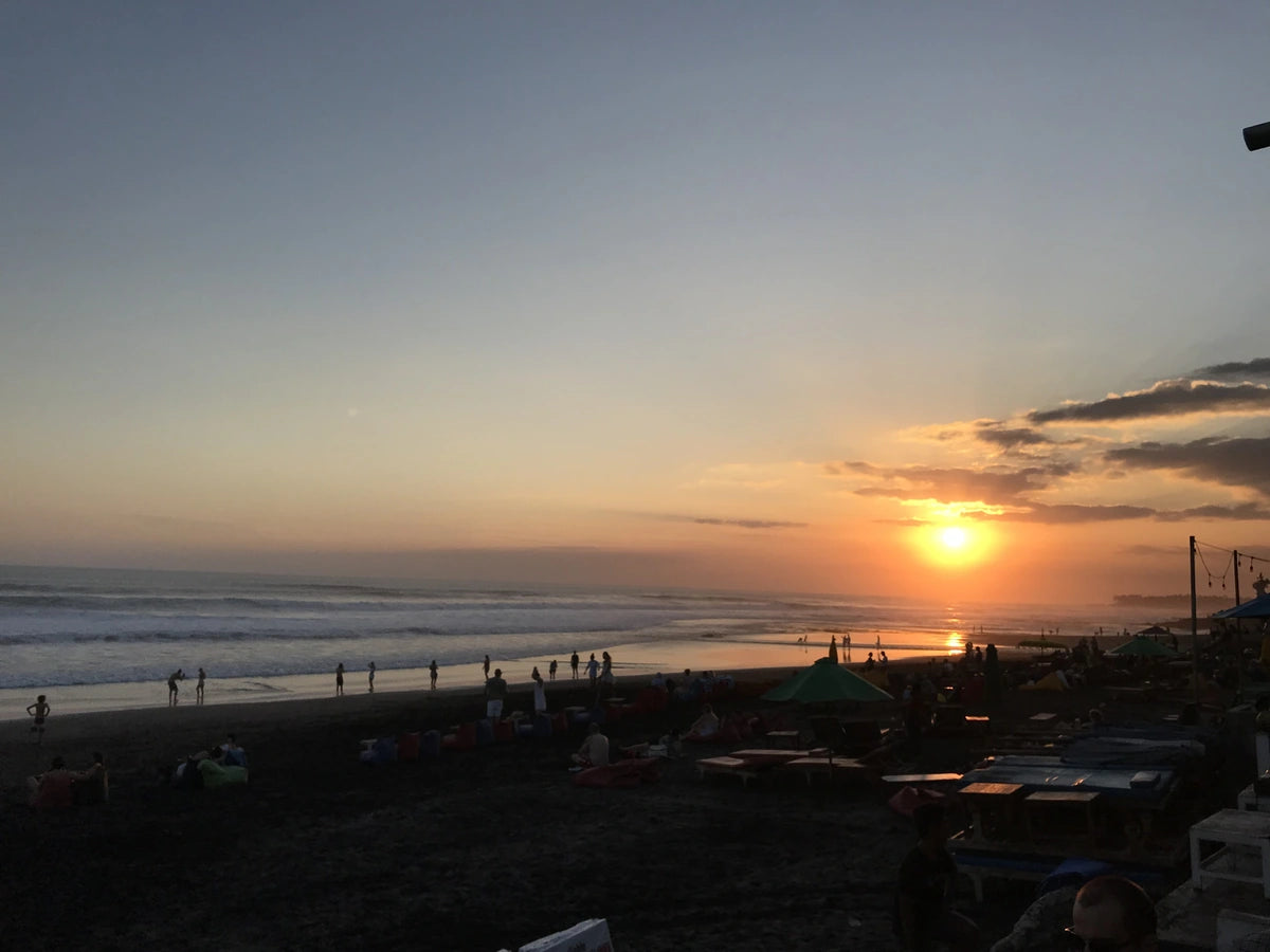 Many tourists on holiday walk along and soak up a beach in Bali with a beautiful sunset on the horizon.