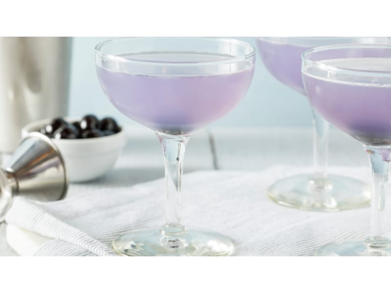 Purple cocktail with jigger and bowl of fruit