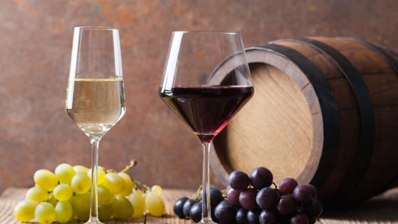 2 filled wine glasses with barrel and grapes on the table