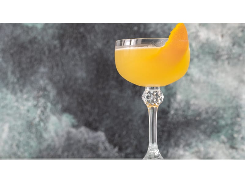 Yellow drink with an orange twist in gray background