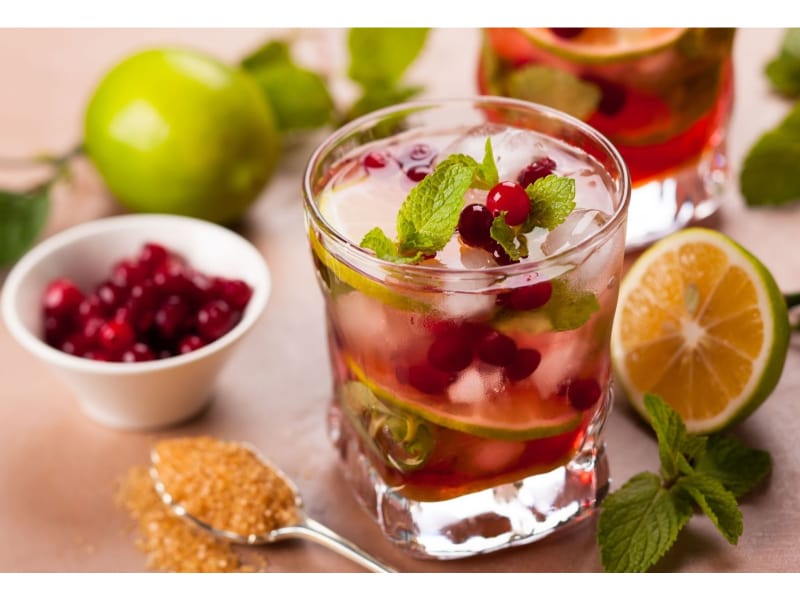 A glass of Virgin Cranberry Mojito with lime, berries, and sugar